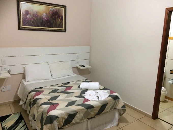 Quarto de casal com colcha estampada, toalhas dobradas e porta para o banheiro