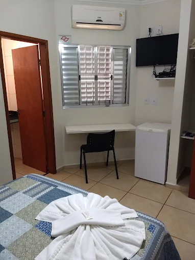 Quarto com ar-condicionado, TV de parede, frigobar e mesa com cadeira